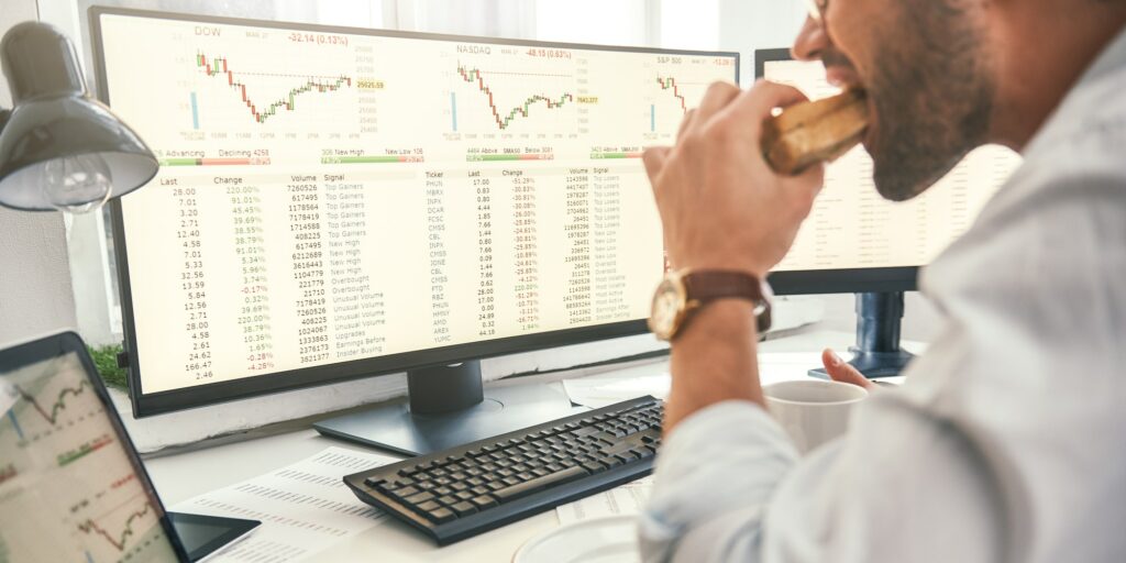 Close-up of bearded trader is eating fresh sandwich with financial data