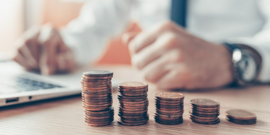 Coin stack in business office, businessman working on laptop computer in background