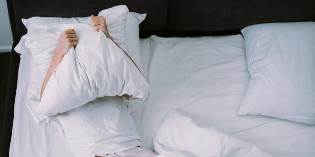 depressed woman covering face with pillow while lying in bed at home