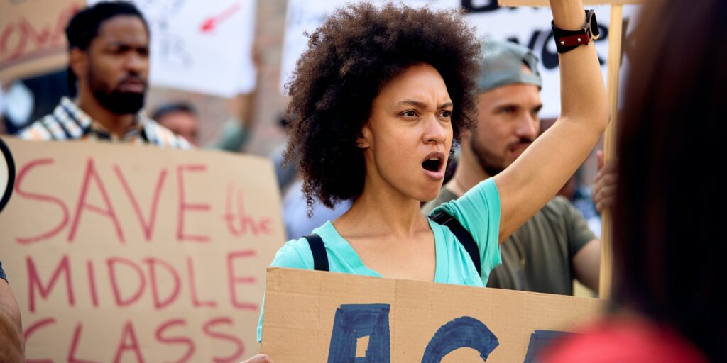 Displeased black woman protesting with group of people against government recession measures.