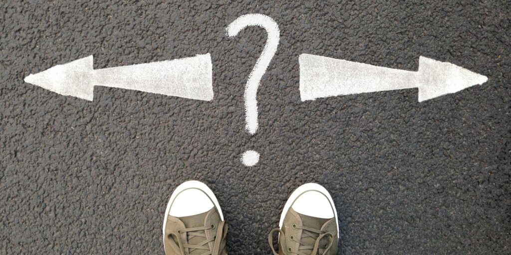 feet standing on street with road markings. question mark between arrows pointing left or right