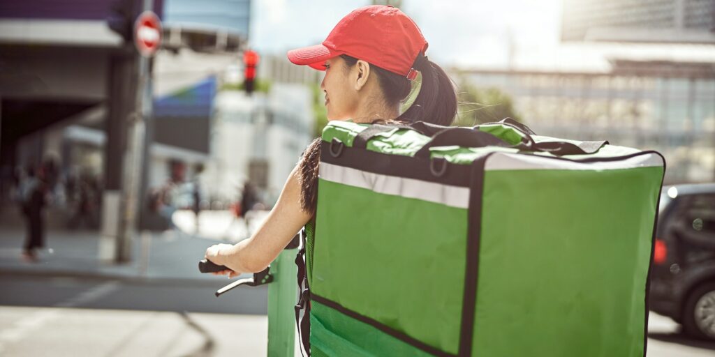Food courier on scooter carrying food delivery bag through city
