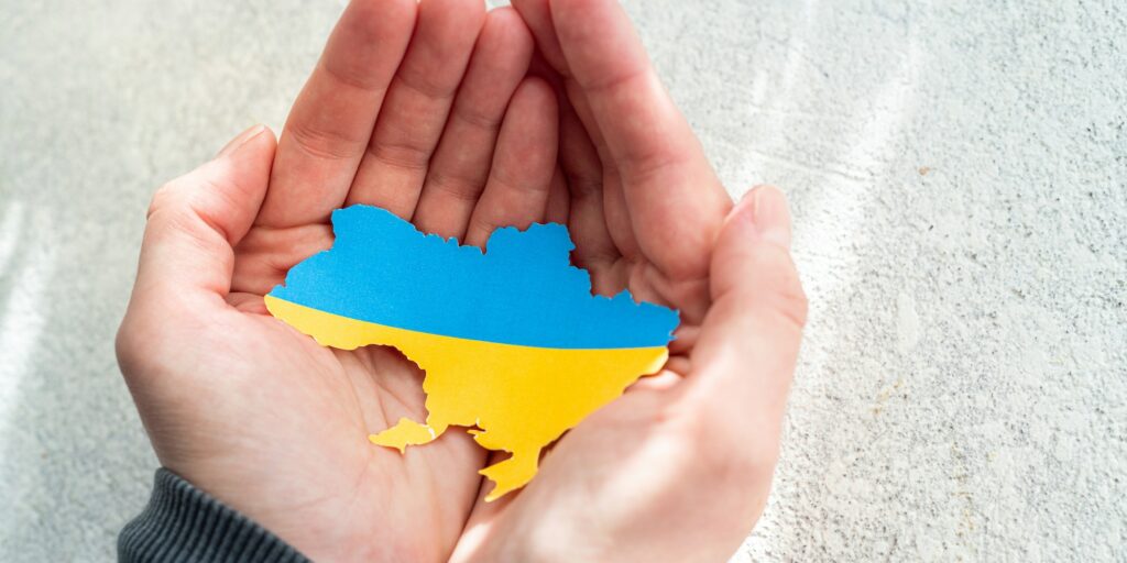 Hands holding national flag of Ukraine in the shape of the borders of Ukraine. Support for Ukraine