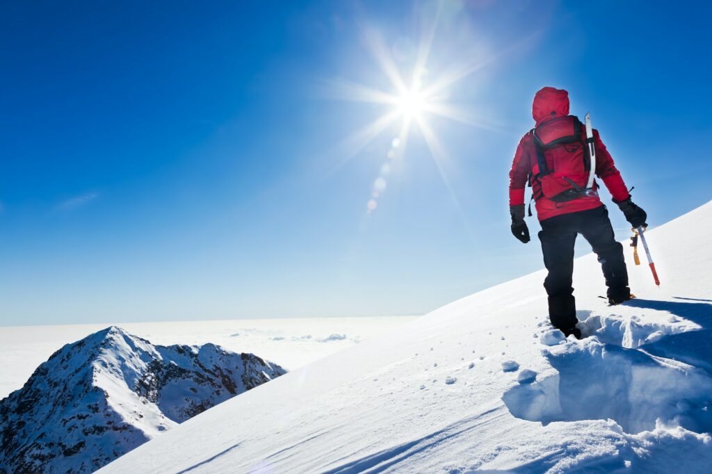 Mountaineer reaches the top of a snowy mountain in a sunny winter day. Western Alps, Biella, Italy.