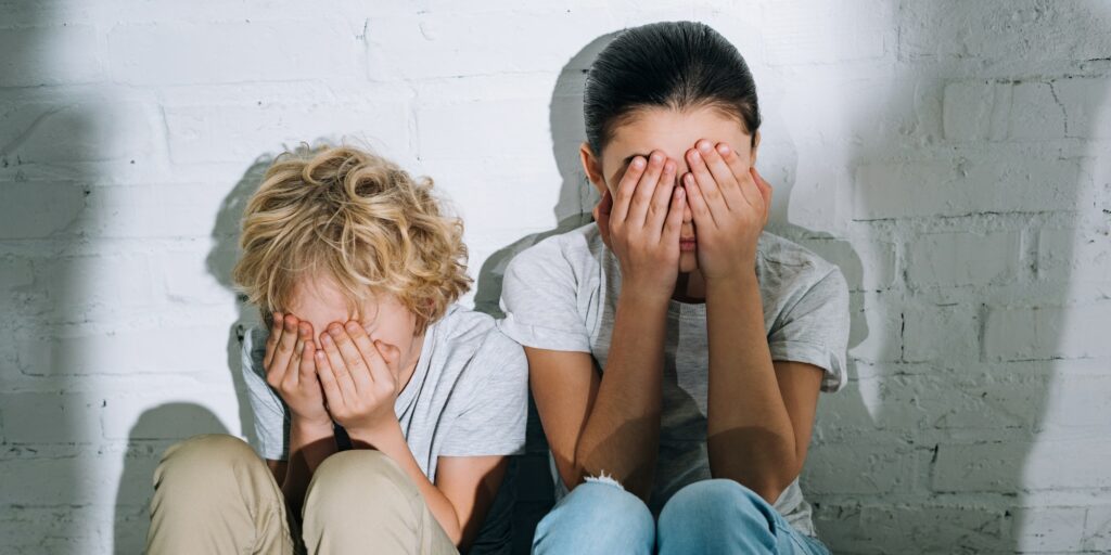 scared children covering eyes with hands while sitting on carpet