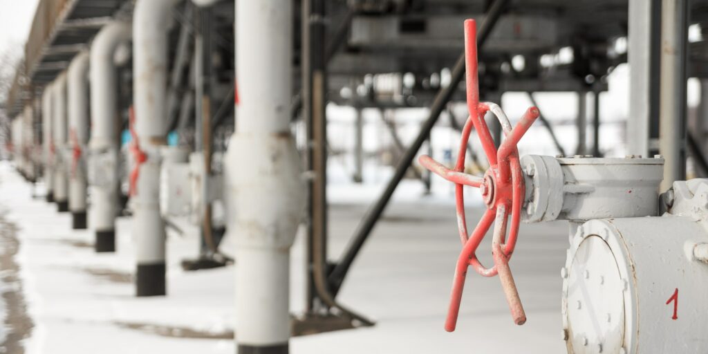 The grey metal tubes for gas delivering with red valves at gas compressor station shooted in winter