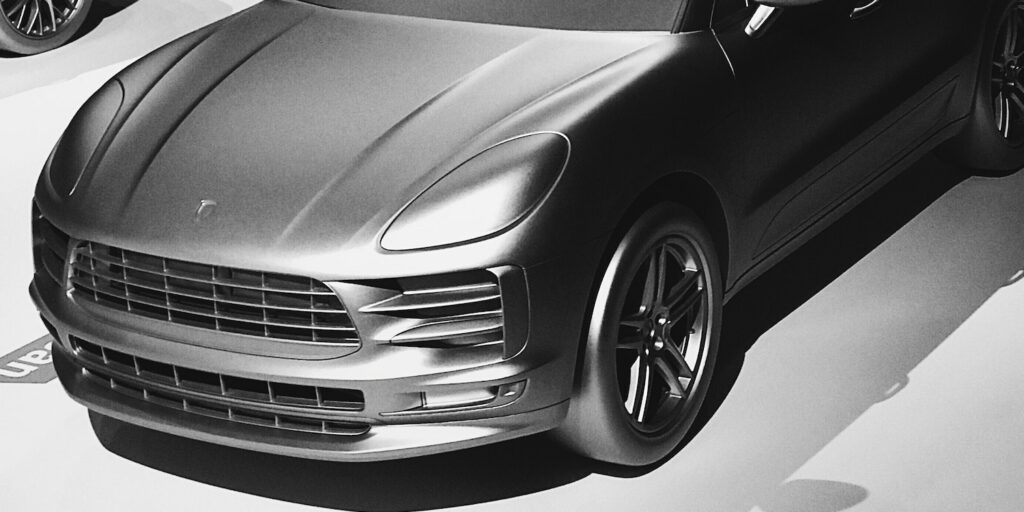 Tiny car models of the brand Porsche driving down a white road