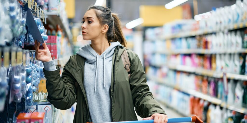 Young woman looking at price tag of hygiene products in supermarket.