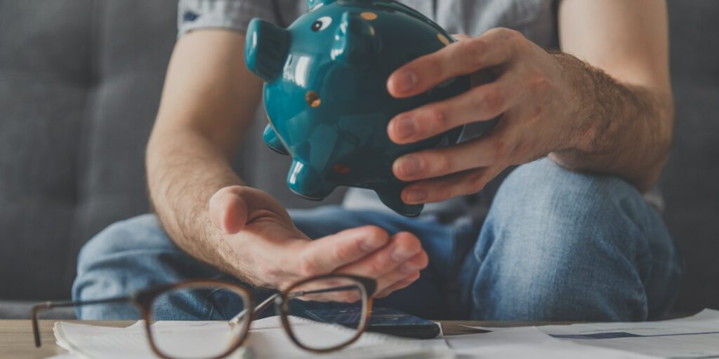 Man sitting at a table full of unpaid bills shakes out the last penny from the piggy bank