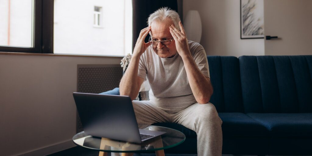 Senior man having headache and touching his head while suffering from a migraine in the living room,
