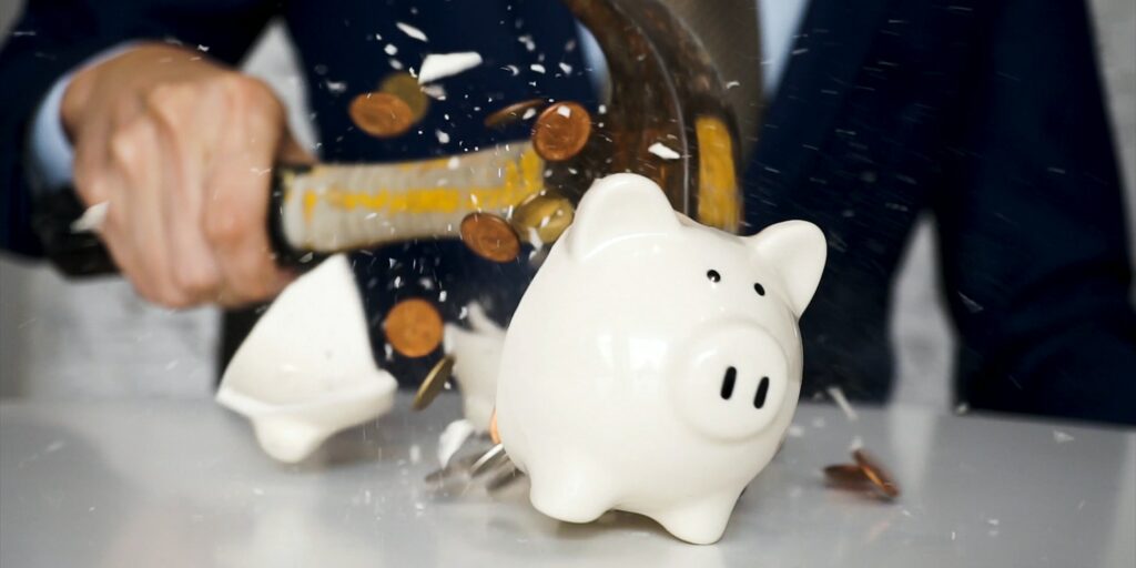 usinessman using a hammer to smash plenty of coins inside piggybank into pieces