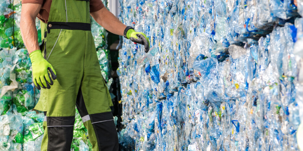 Waste Management Worker in Front of a Pile of Pressed Plastic PET Bottles