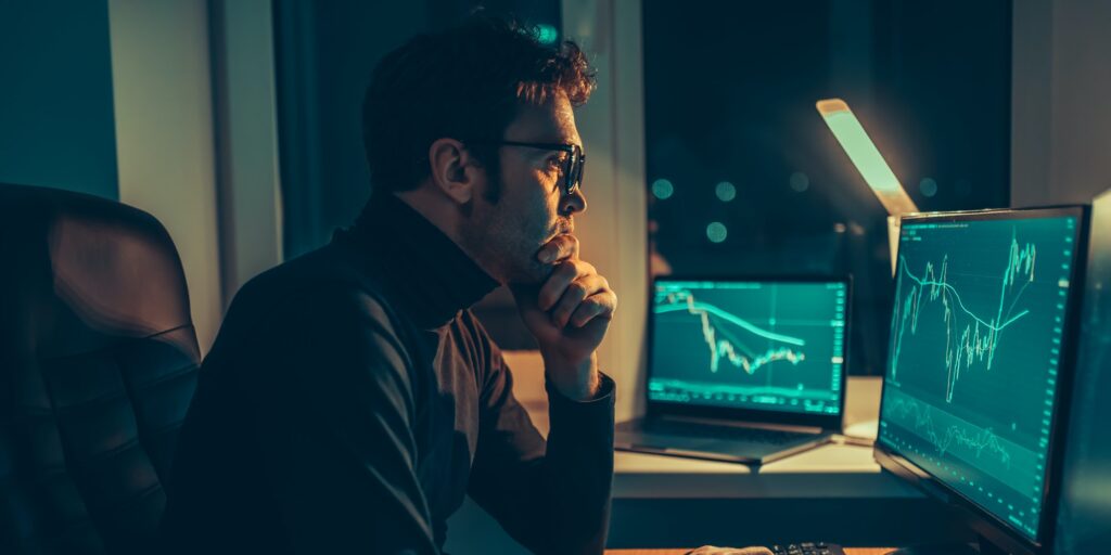 Analyzing the Market In a dimly lit home office, a male trader reviews charts and indexes,