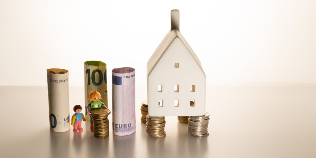Coins and banknotes next to a small miniature house and miniature figures
