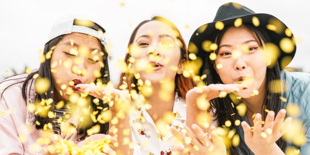 Happy Asian friends doing party throwing confetti outdoor