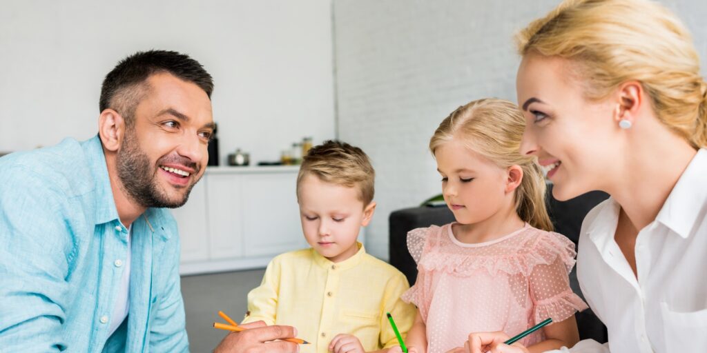 happy parents with two little kids drawing with colored pencils at home