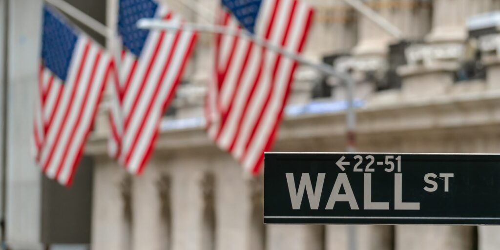 Wall Street "WALL ST" sign and broadway street over American national flags