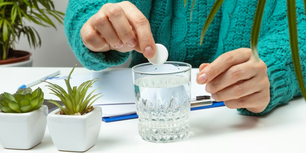 Woman sits at the table and throws a round aspirin into the sakan with water, headache