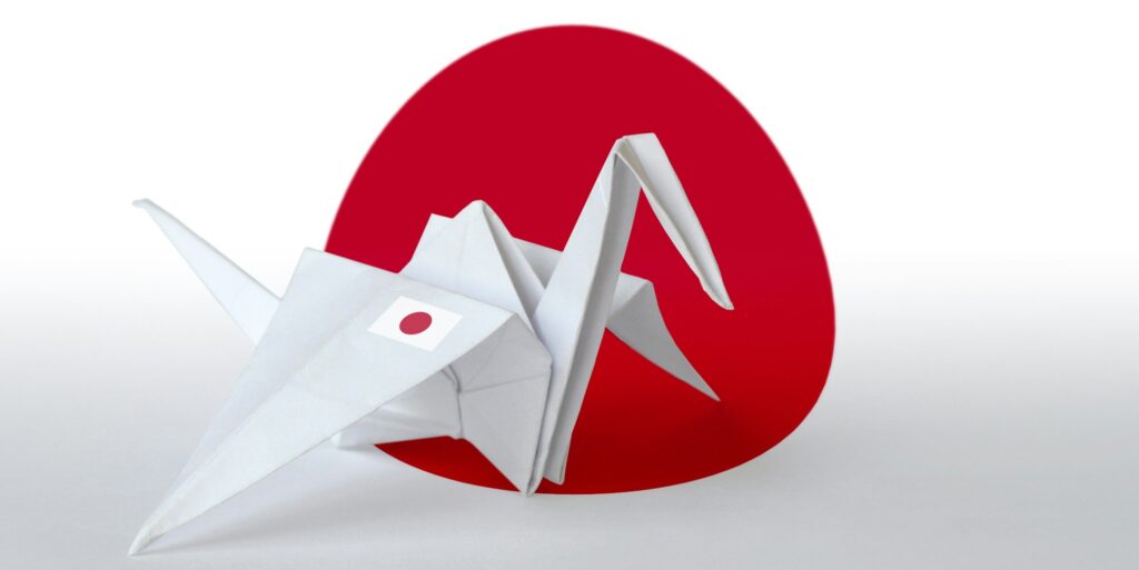 Japan flag depicted on paper origami crane wing. Oriental handmade arts concept