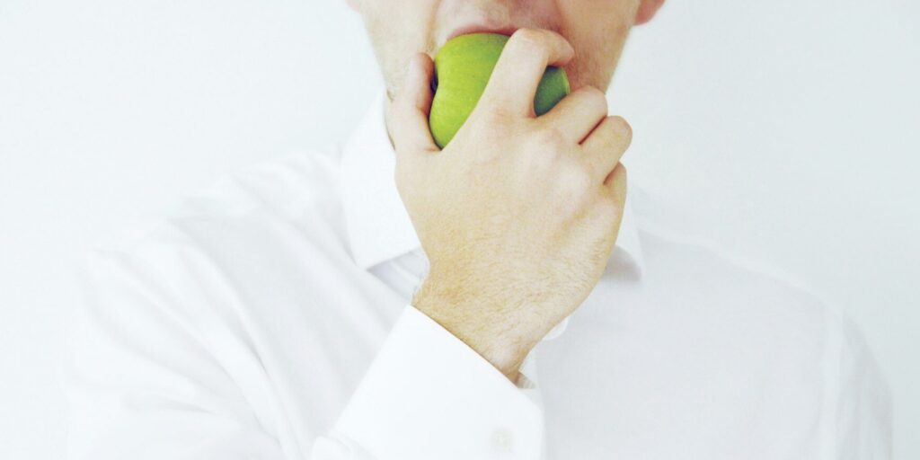 Photo of a businessman taking a bite of a green healthy apple