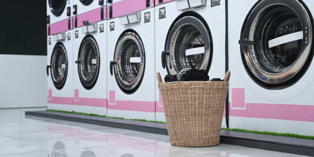 A basket of laundry near row of washing machines. Self service laundry facilities.