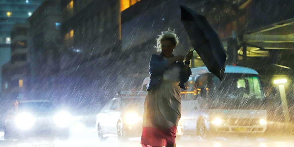 A millennial girl struggling with the umbrella in the heavy rain during the night.