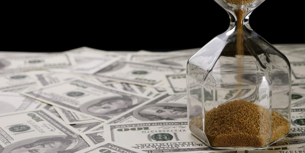 Brown sand pouring in clear sandglass on banknotes
