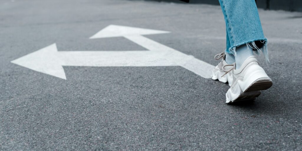 cropped view of woman in jeans walking near directional arrows on asphalt