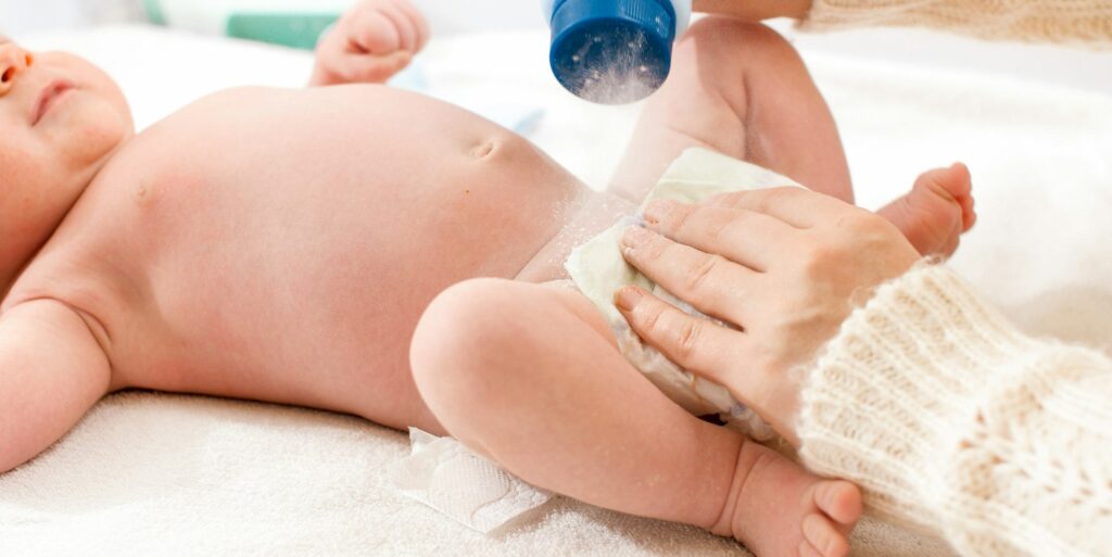 Closeup of mother applying talcum powder while changing messy diapers of her little baby son on