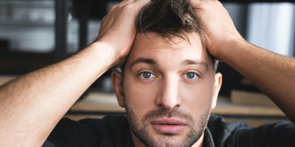 handsome man with panic attack touching head in apartment