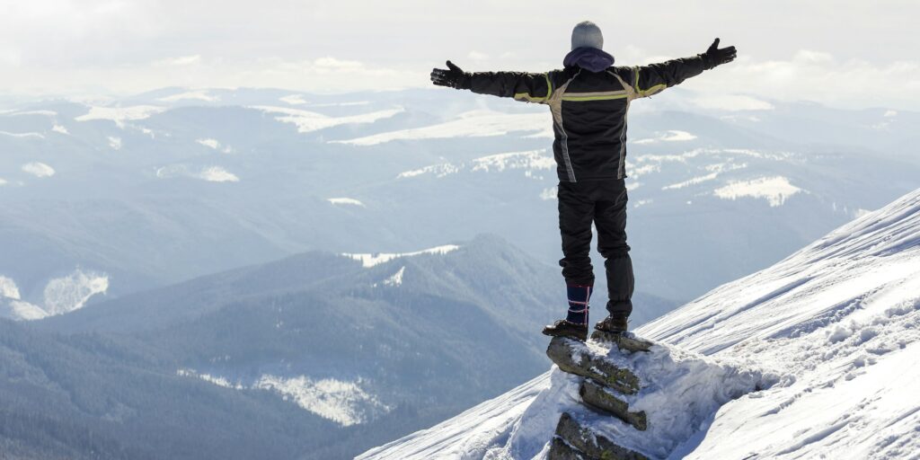 Silhouette of alone tourist standing on snowy mountain top in winner pose