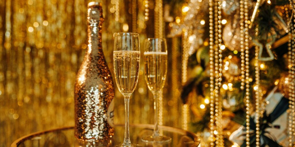 Champagne glasses and bottle against luxe glow golden rain decoration for expensive holidays party