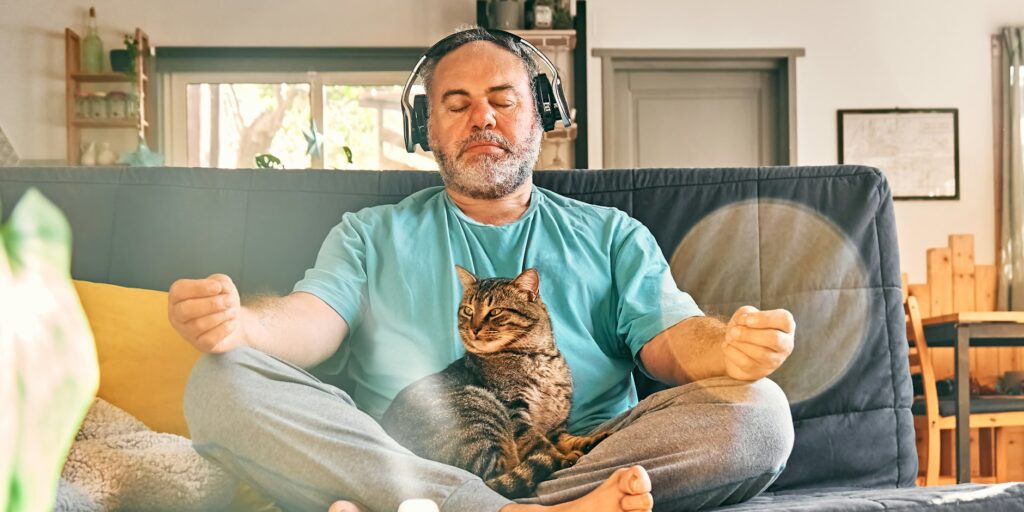 Mature middle-aged overweight man in wireless headphones meditation at home with his cat.
