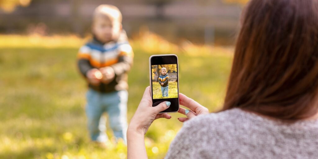 mom takes pictures of her baby on a smartphone in an autumn park