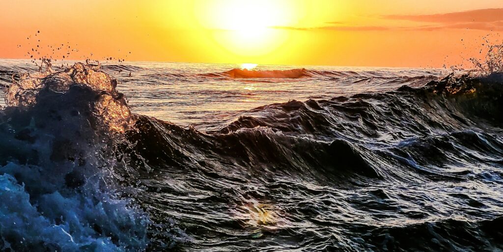 Ocean waves crashing a sea with beautiful sky of orange reflected in turbulent water.