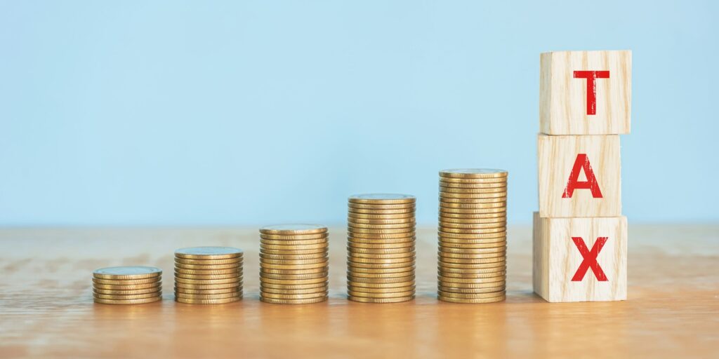 Up golden coin stack on wooden desk with word "TAX" on wood block.