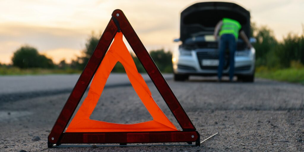 Broken silver luxury car emergency accident. Man driver installing red triangle stop sign on road