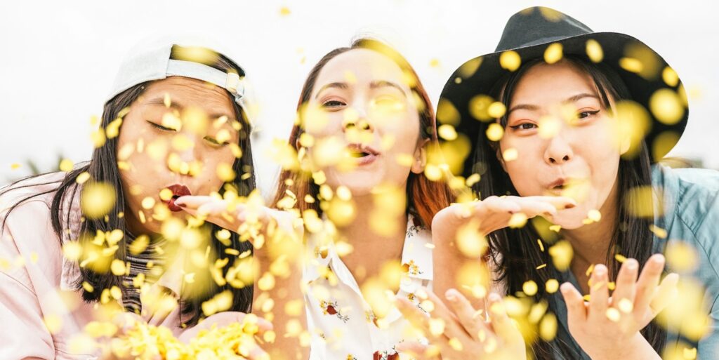 Happy Asian friends doing party throwing confetti outdoor