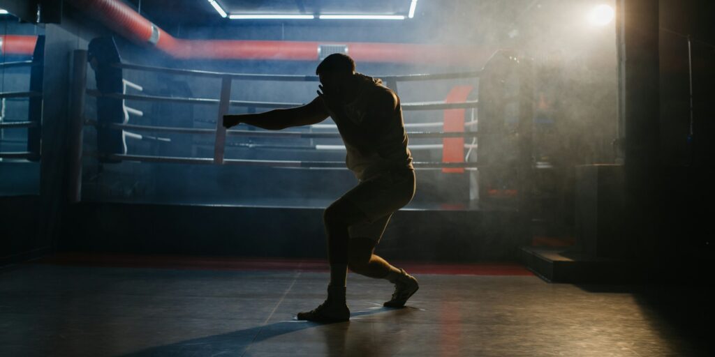 A male boxer is boxing with a shadow on the background of a boxing ring.