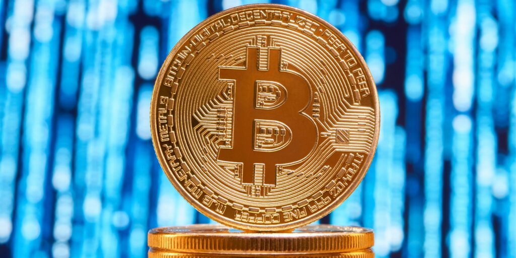 One bitcoin on edge placed on stack of golden bitcoins with blurred blue circuit on background