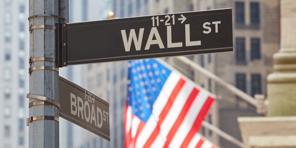 Wall Street sign near Stock Exchange with US flags, New York