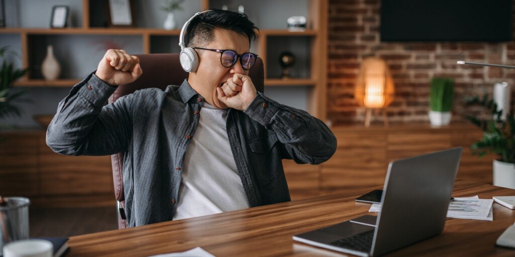 Tired boring adult korean man manager in glasses and headphones yawns and rests from work