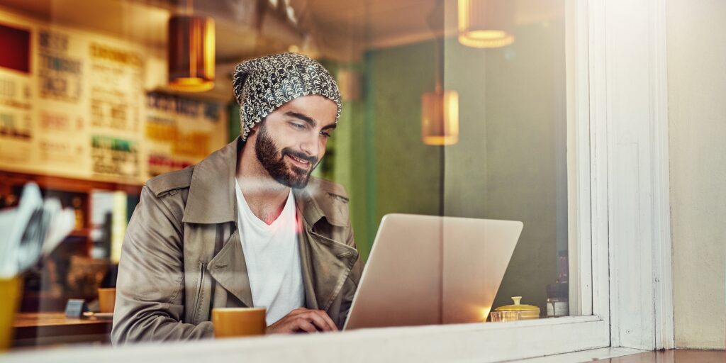 Shot of a handsome young man sitting at a cafe counter using a laptop