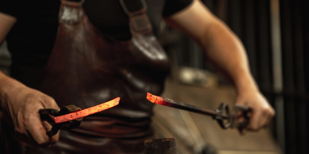 Close-up working powerful hands of male blacksmith forge an iron product in a blacksmith. Hammer