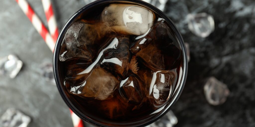 Glass of cola, ice and straws on black smokey background