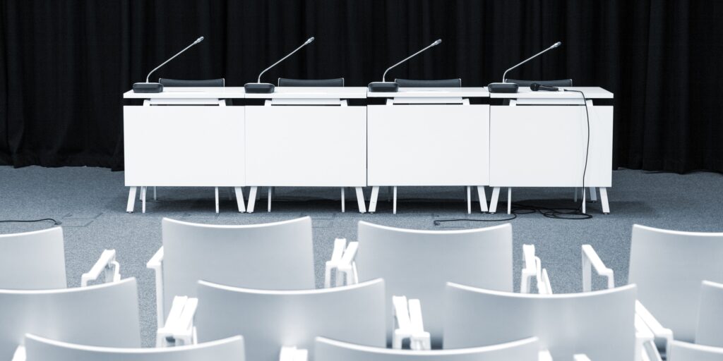 Monochrome picture of empty press conference room with seats, stand table and microphones