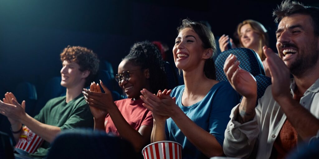 Happy spectators applauding after movie projection in cinema.