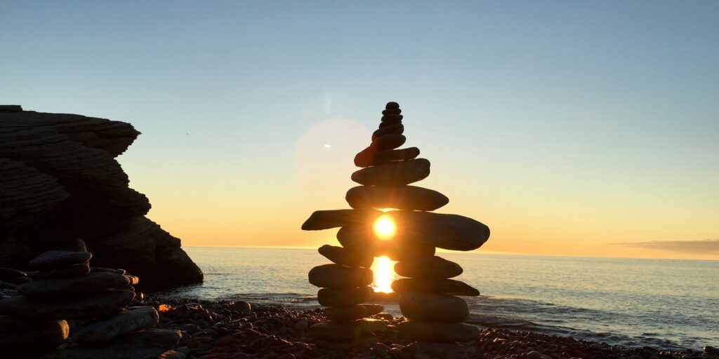 Inukshuk sculpture built at the edge of ocean and glowing in the rays of rising sun