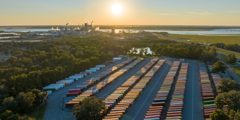 Aerial view of large cargo container yard with rows of freight containers and big factory