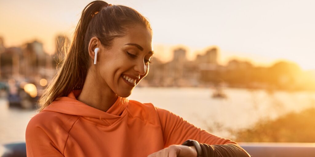 Happy sportswoman using fitness tracker while exercising at sunset.